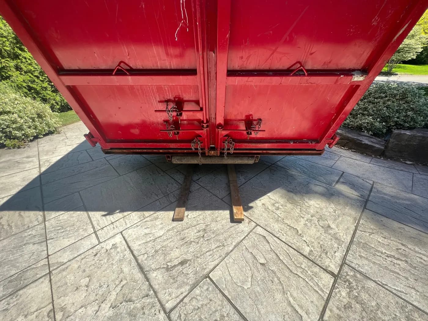 Wood planks laid under an AG Disposal bin on a stone driveway